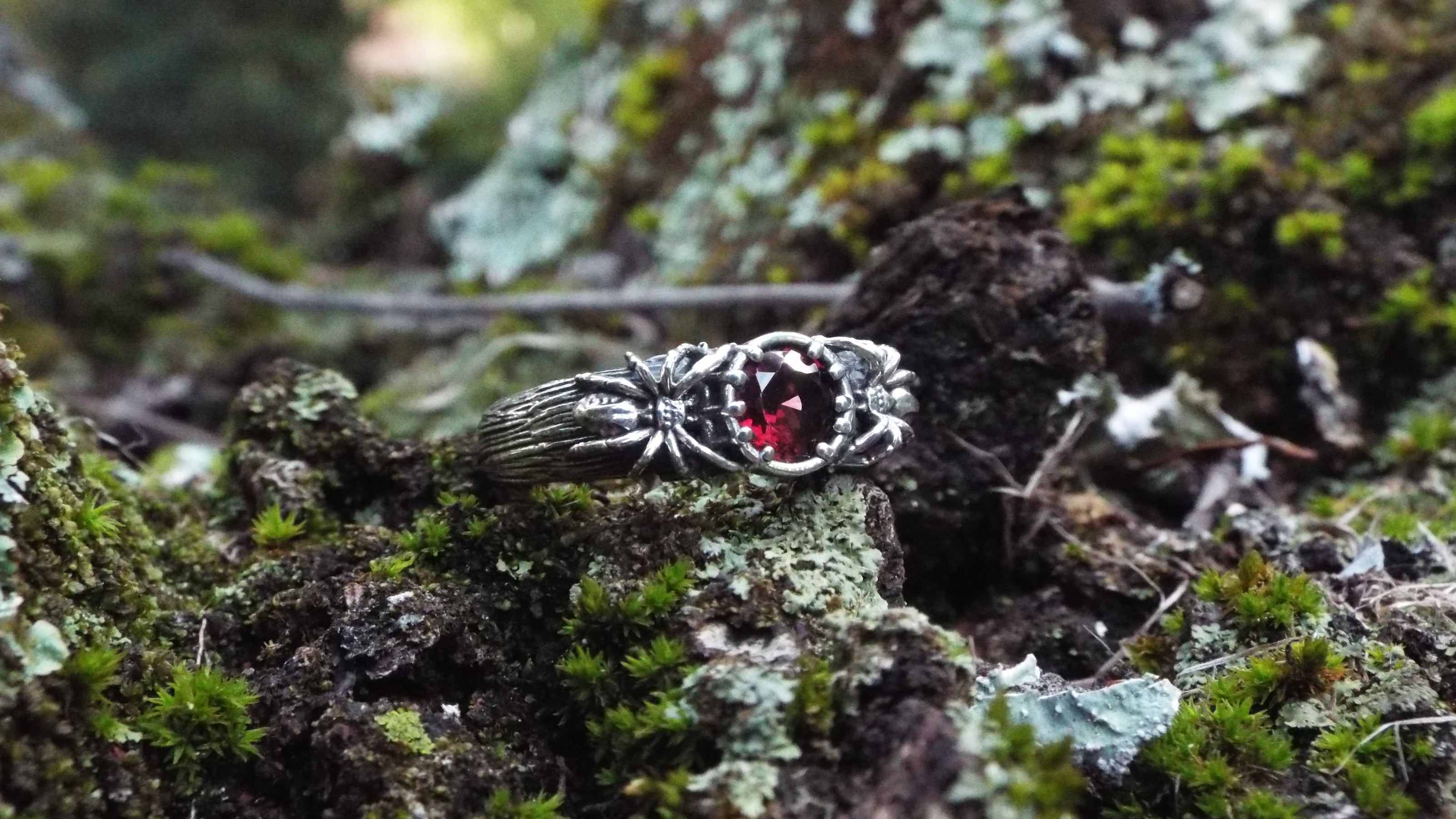 Silver Spider ring with a red Garnet gemstone on a mossy surface