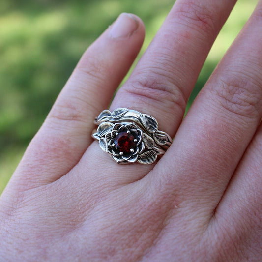 A sterling silver bridal ring with a garnet lotus design, displayed on a person's hand.